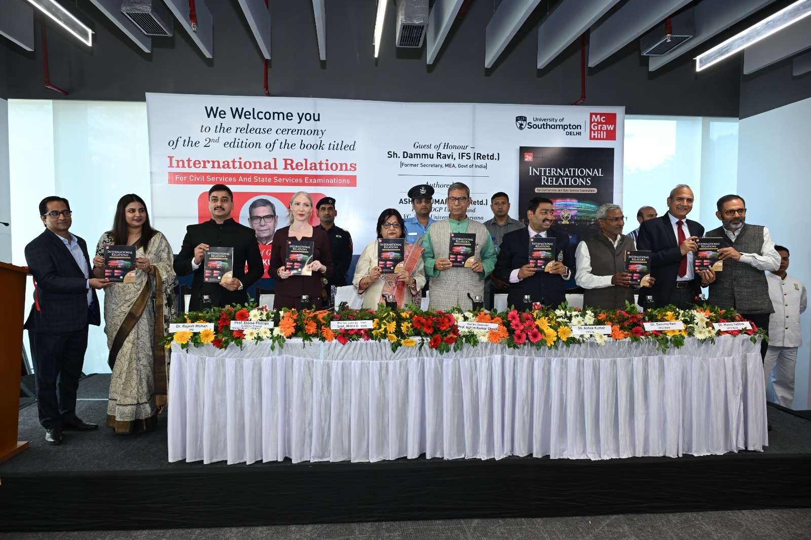 Academic and professional staff at the launch of a book standing behind a table decorated with flowers