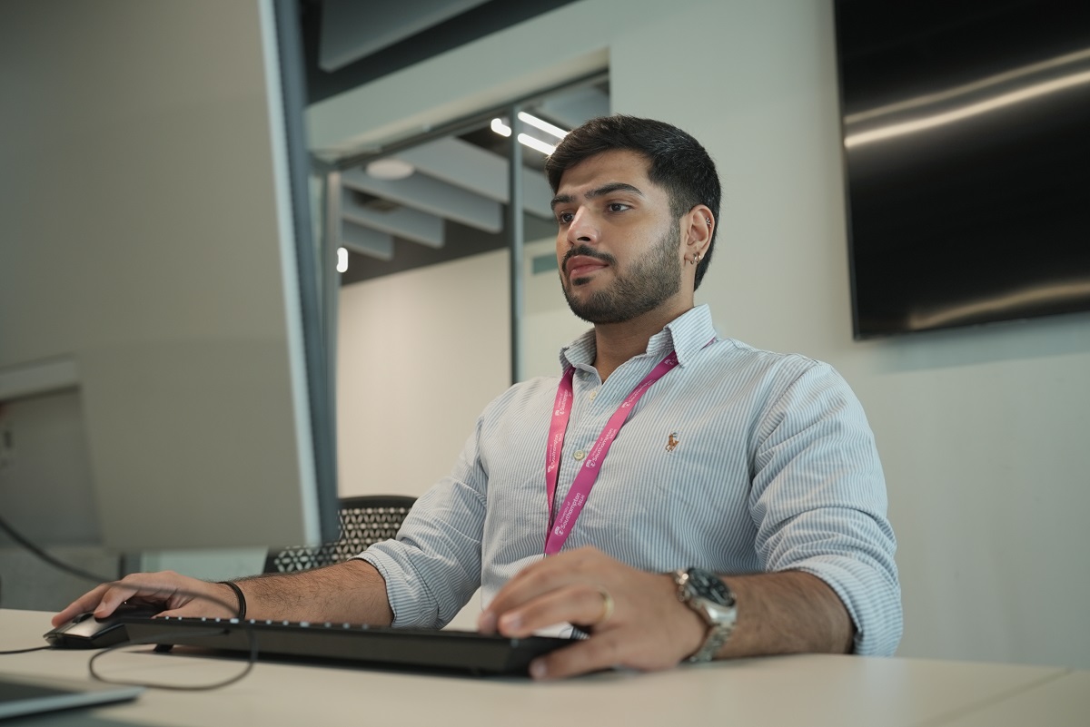 A student sits at a desk using a keyboard looking slightly to the left of camera where a monitor would be