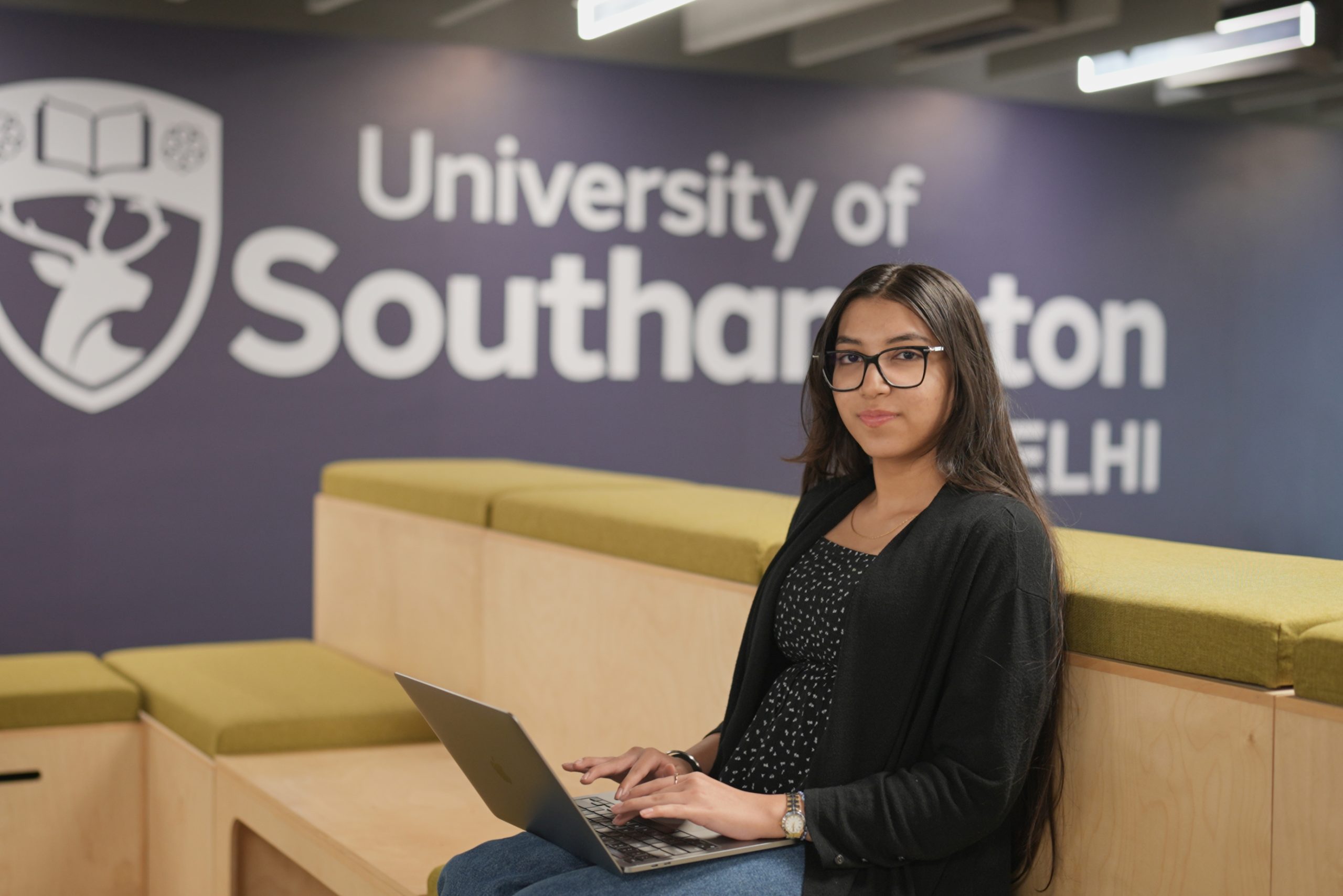A Business Management BSc (Hons) degree student sits and looks towards camera as they use a laptop