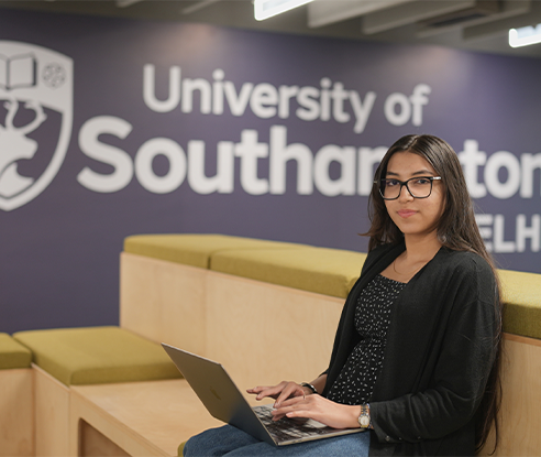A Business Management BSc (Hons) degree student sits and looks towards camera as they use a laptop